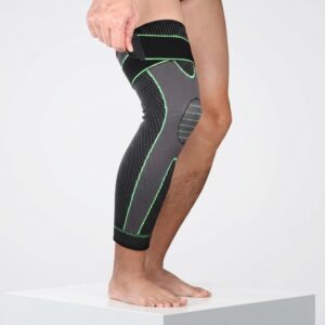 A side profile of a person's leg wearing a black and grey compression knee sleeve with adjustable strap and green accents.