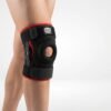 Close-up of a bare leg wearing a black and red Mana NEO-8002 neoprene hinged knee brace with an open patella cutout.